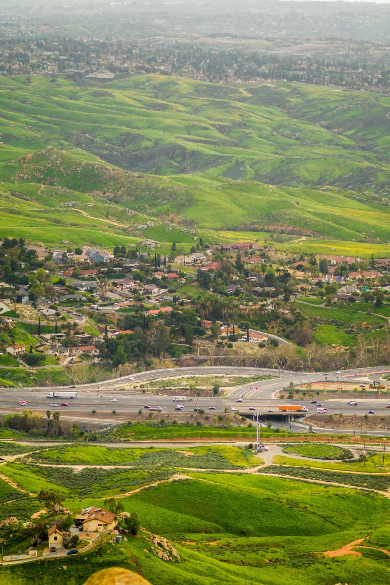 Green hills with houses scattered across the slopes, above a freeway crossing the valley floor.
